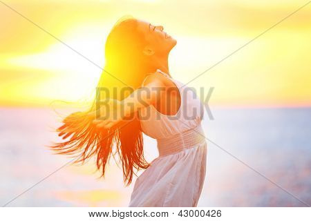 Picture or Photo of Enjoyment - free happy woman enjoying sunset. Beautiful woman in white dress embracing the golden sunshine glow of sunset with arms outspread and face raised in sky enjoying peace, serenity in nature