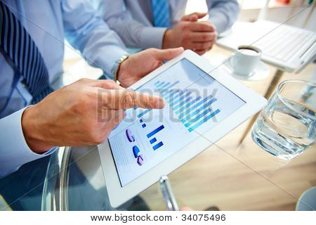 Picture or Photo of Modern people doing business, graphs and charts being demonstrated on the screen of a touch-pad