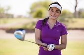 image of golf  - Cute Hispanic female golfer holding a golf club with both hands and smiling - JPG 