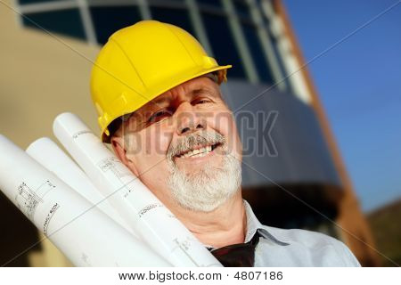 Picture or Photo of Architect with blueprints in a hardhat in front of a modern building