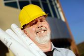 stock photo of construction worker  - Architect with blueprints in a hardhat in front of a modern building - JPG 