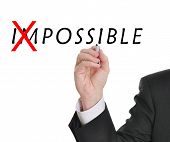 picture of possibility  - Businessman in suit drawing text of the word impossible with red mark through part of the word making it now possible - JPG 