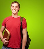 pic of young adult  - portrait of a young student holding a book and carrying a backpack over a green background - JPG 