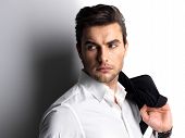 picture of contrast  - Fashion young man in white shirt holds the black jacket over wall with contrast shadows - JPG 