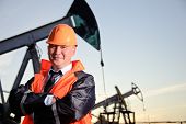 stock photo of industrial  - Oil worker in orange uniform and helmet on of background the pump jack and sunset sky - JPG 