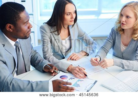 Picture or Photo of Two employees listening to the business partner while working with papers at meeting