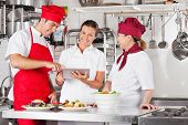 image of computer  - Female chef with colleagues looking for recipe on a tablet computer while cooking at kitchen - JPG 