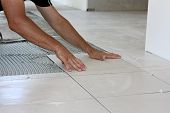 stock photo of tiles  - a male tiler laying light color floor tiles - JPG 