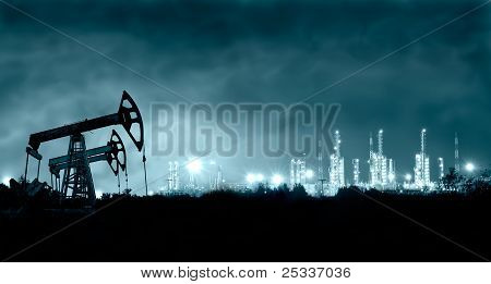 Picture or Photo of Group oil rigs and brightly lit industrial site at night. Toned.
