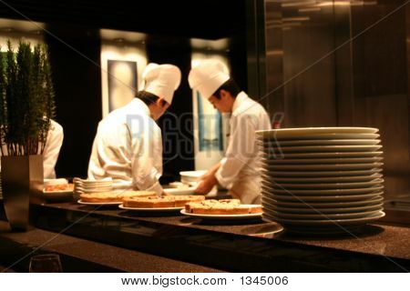 Picture or Photo of Two chefs working in a busy restaurant kitchen with tasty food cooling in the foregound.