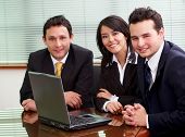 stock photo of meeting  - businessmen and businesswomen in a business meeting in an office smiling with a laptop on the table - JPG 