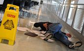 image of depth  - A man who slipped on a wet floor beside a bright yellow caution sign holds his back in pain
 - JPG 