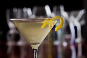 stock photo of depth  - dirty martini chilled and served on a busy bar top with a shallow depth of field and color lights and glasses in the background garnished with a lemon twist
 - JPG 