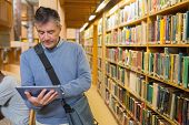 stock photo of man  - Man holding a tablet pc amongst shelves in a library - JPG 
