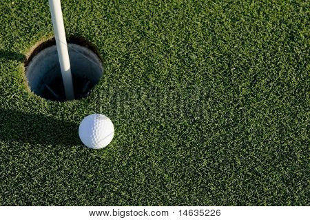 Picture or Photo of A white golf ball near the hole of a golfing green or course
