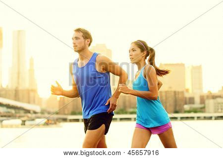 Picture or Photo of City running couple jogging outside. Runners training outdoors working out in Brooklyn with Manhattan, New York City in the background. Fit multiracial fitness couple, Asian woman, Caucasian man.