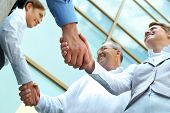 image of handshake  - Below view of rows of happy partners handshaking outdoors on background of modern building - JPG 
