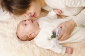 Mother and newborn daughter lie on a pink plaid. They are dressed in warm knitted white sweaters. Mother and child face to face