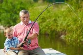 stock photo of youngster  - Photo of grandfather and grandson pulling rod together while fishing - JPG 