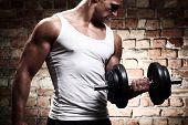 stock photo of health  - Muscular guy doing exercises with dumbbell against a brick wall - JPG 