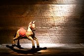 foto of horse  - Nostalgic Americana scene of an antique reproduction wood toy rocking horse on aged wooden plank floor in a dusty old house attic lit by soft diffused sunlight through a window - JPG 