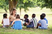 picture of education  - Children and education young woman at work as educator reading book to boys and girls in park - JPG 