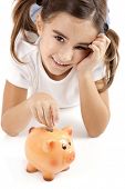 stock photo of insert  - Little girl lying on floor and inserting a one euro coin on the piggy - JPG 
